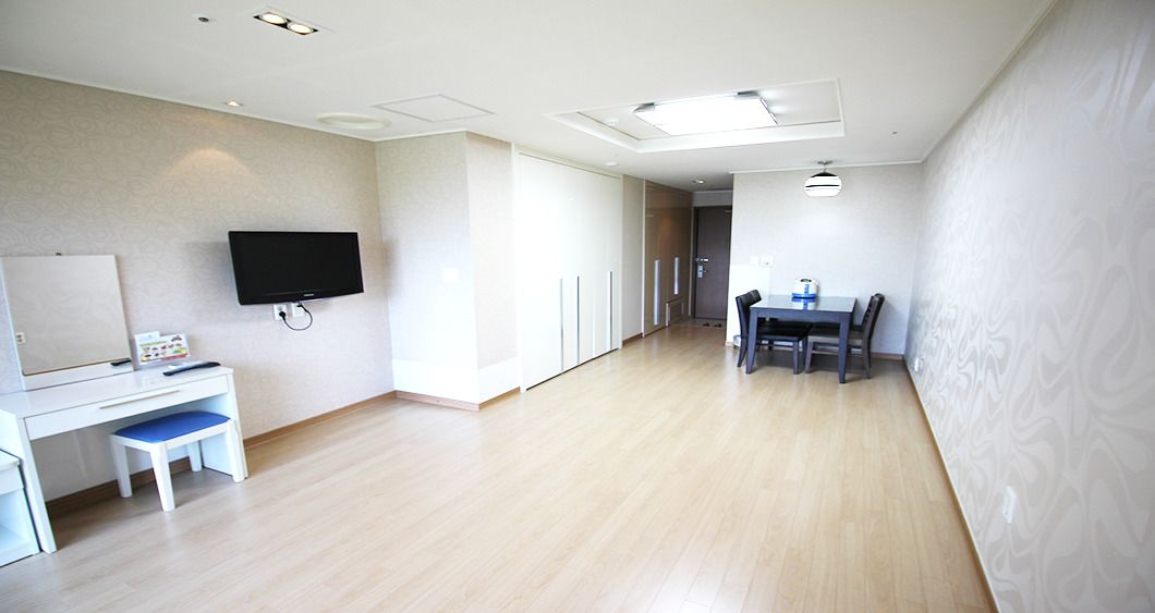 A modern hotel room with a flat-screen TV mounted on the wall, a desk with a chair, and a dining area with a table and chairs.