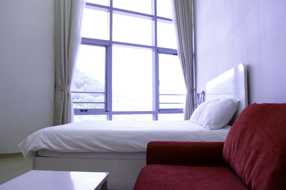 A single bed with white bedding, a red sofa, and a window with curtains.