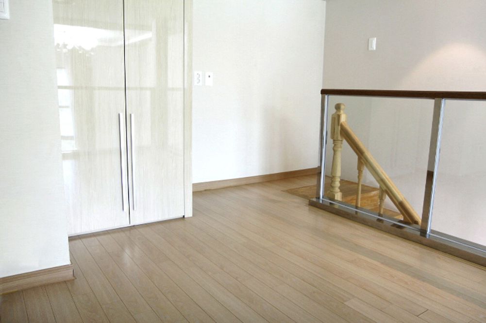 Una habitación con piso de madera, un armario blanco y una barandilla de vidrio con escaleras de madera.