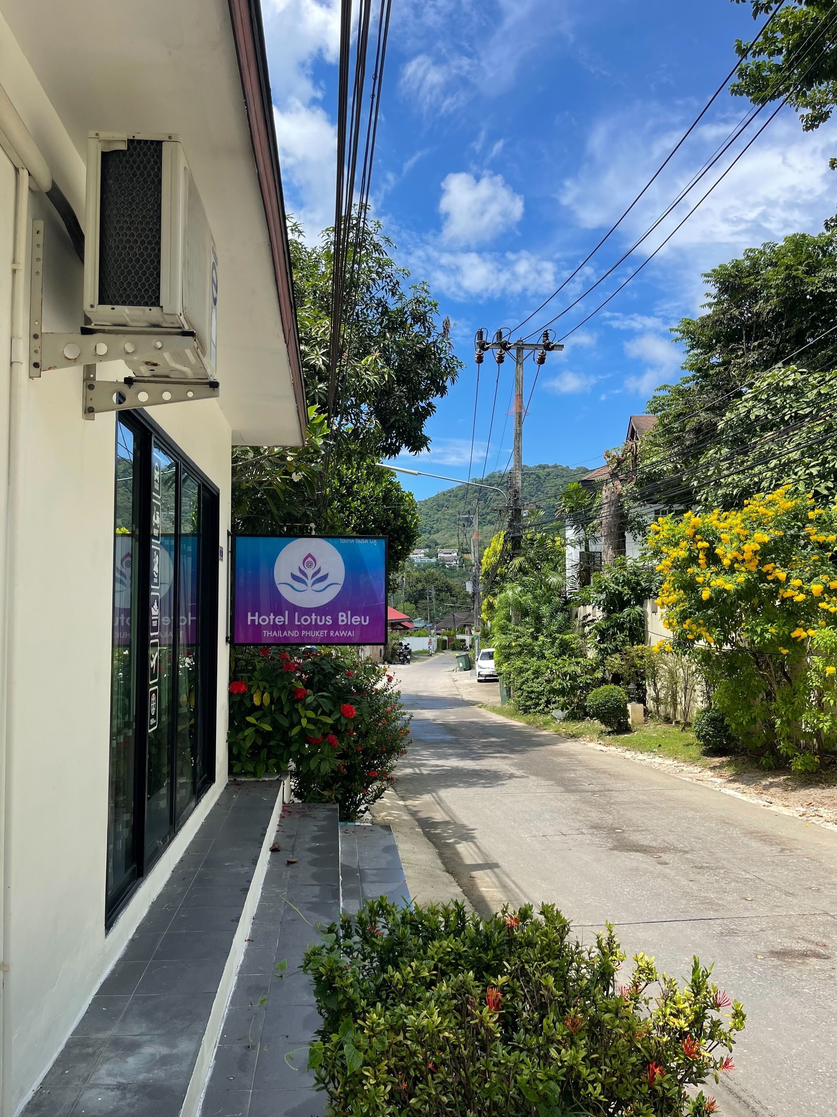 A hotel entrance with a sign for Hotel Lotus Bleu, surrounded by greenery and a clear sky.
