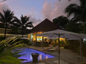 A pool area with lounge chairs and umbrellas, a bar, and a building with a red roof. - Lotus Bleu Resort & Restaurant (Rawai)