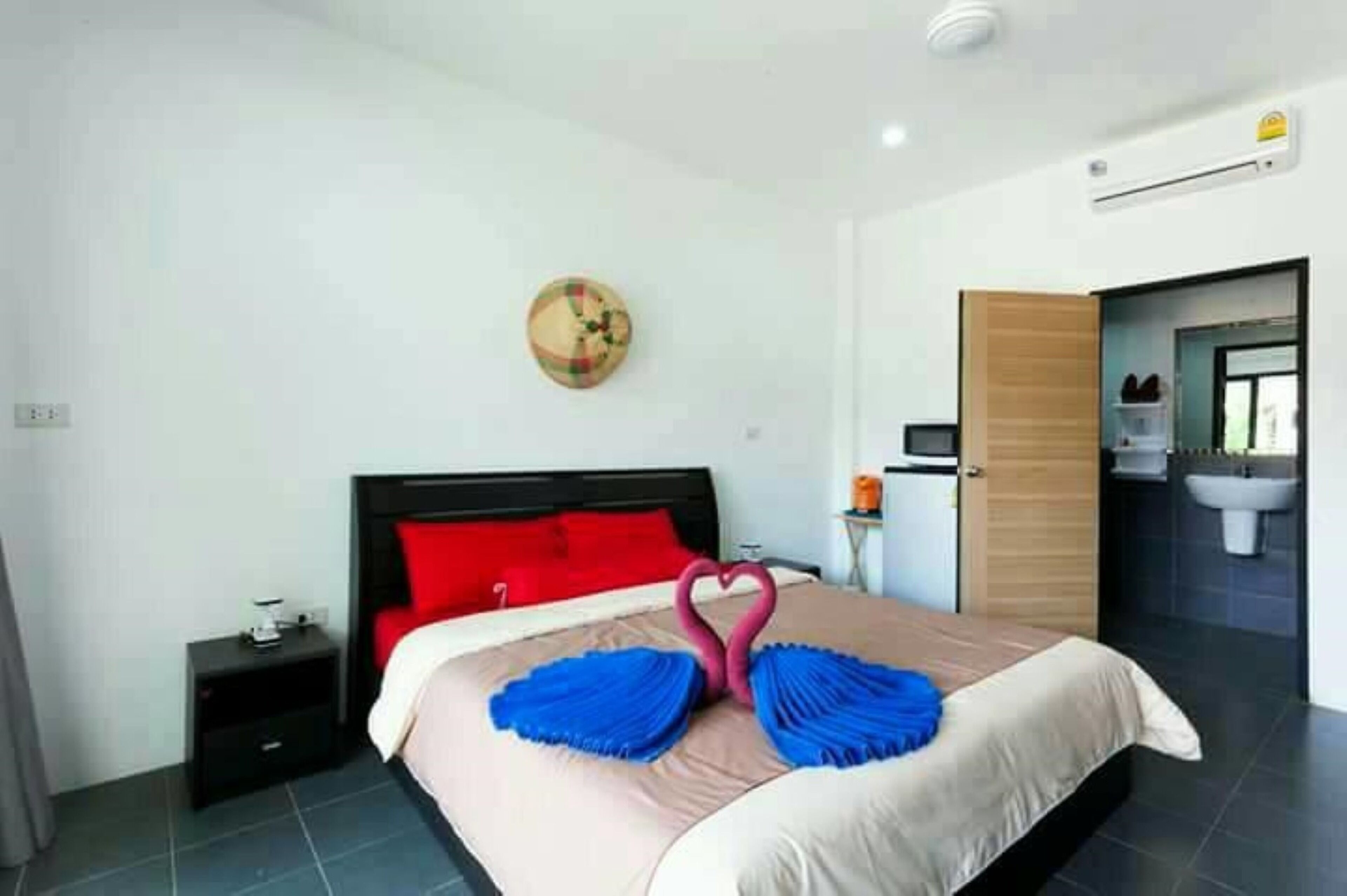 Een moderne hotelkamer met een keurig opgemaakt bed, een klein nachtkastje, een wandklok en een badkamer zichtbaar door een geopende deur.