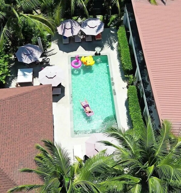 A rectangular swimming pool with a person floating on a floatation device. Surrounding the pool are several lounge chairs and umbrellas. - Lotus Bleu Resort & Restaurant (Rawai)