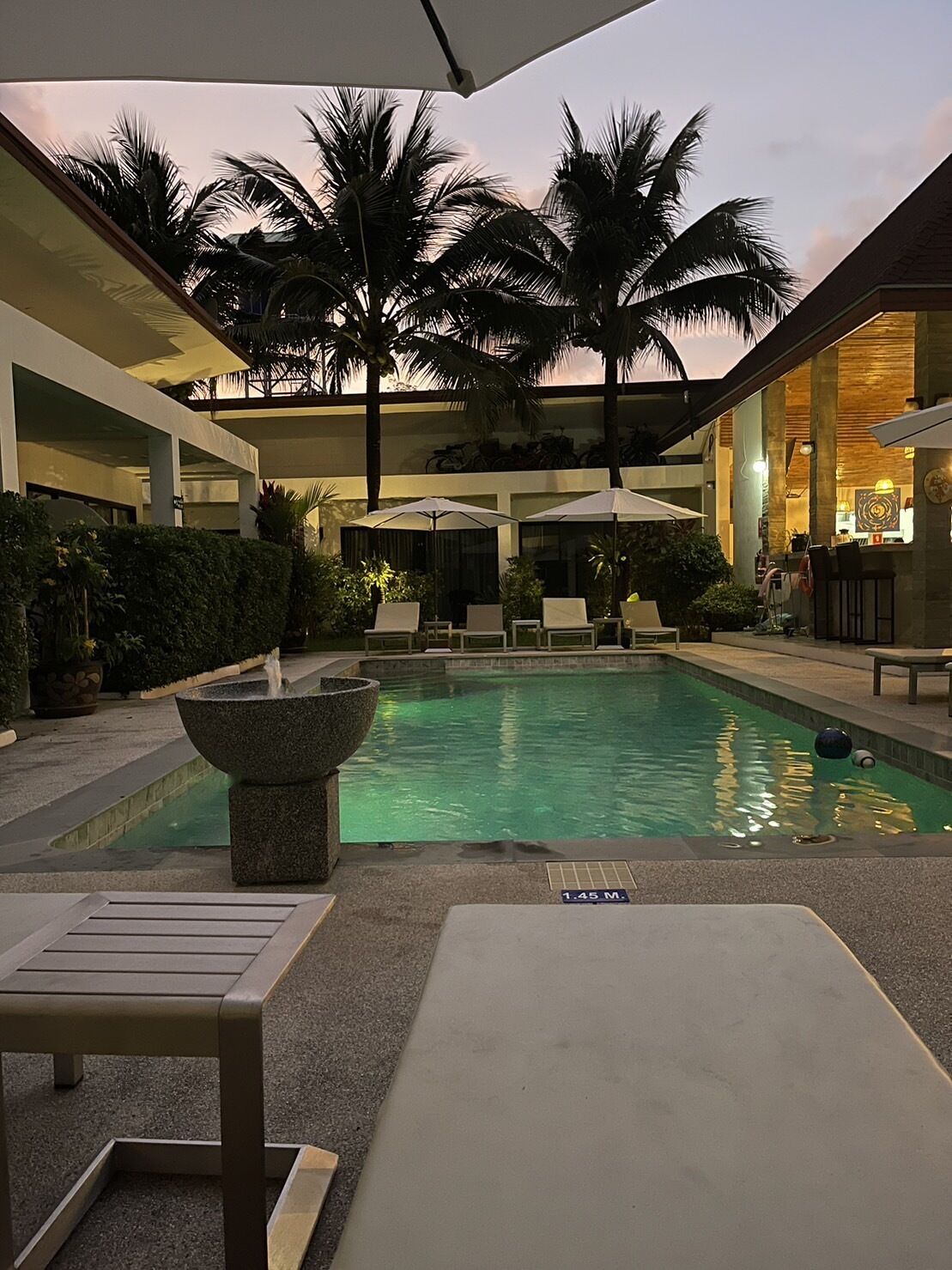 A pool area with lounge chairs, umbrellas, and a water feature.