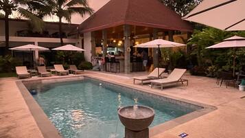 A pool area with lounge chairs, umbrellas, and a covered seating area.