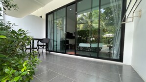 A modern outdoor area with a glass door leading to a patio, a dining table with chairs, and a TV mounted on the wall. - Lotus Bleu Resort & Restaurant (Rawai)