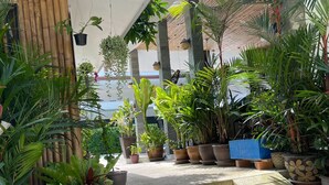 A covered outdoor area with steps leading up to a building, surrounded by various potted plants and a bamboo fence. - Lotus Bleu Resort & Restaurant (Rawai)