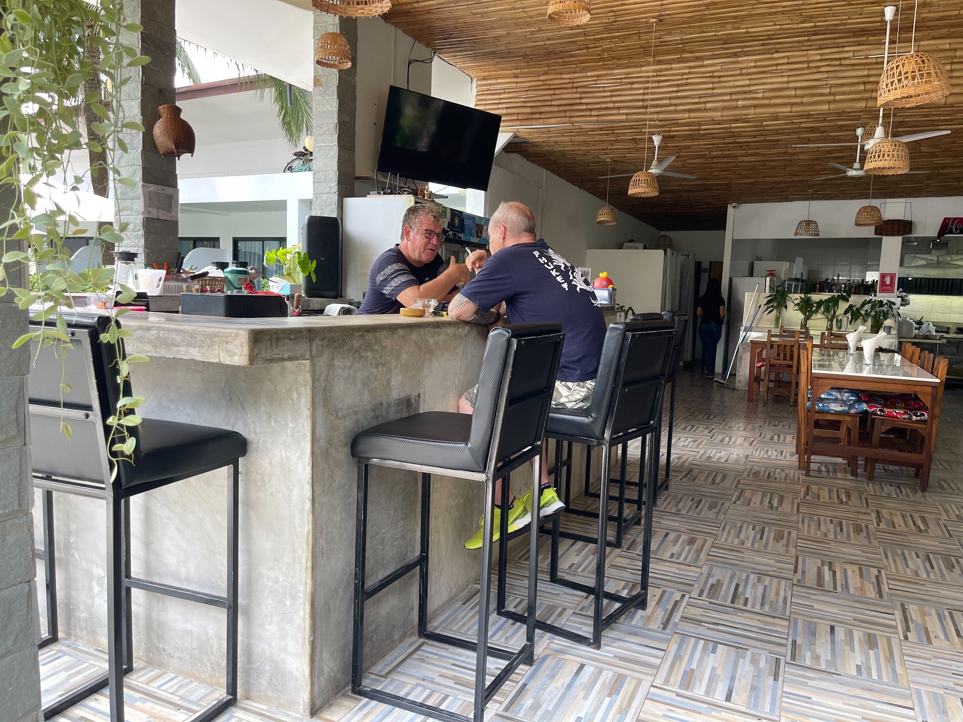 Zona de bar con mostrador de concreto, taburetes negros y un televisor montado en la pared.