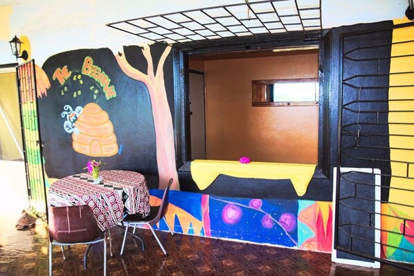 A room with a mural, a table with a yellow tablecloth, and a chair. - The Beehive Fiji (Rakiraki)