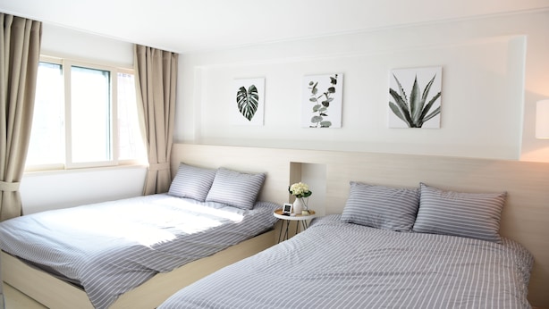 A modern bedroom with two beds, a bedside table with a vase, and wall art. - JW STAY in HONGDAE - Hostel (Seoul)