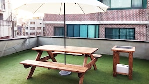 A rooftop terrace with a wooden picnic table and a small table, surrounded by a white umbrella. - JW STAY in HONGDAE - Hostel (Seoul)