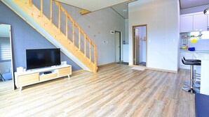Un salon moderne avec un escalier en bois, un téléviseur à écran plat et un coin cuisine équipé de tabourets de bar.