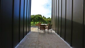 Un balcon avec une table et des chaises, une vue sur la verdure et la façade d’un immeuble moderne.