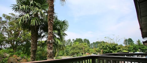 A wooden deck with a railing overlooking a lush garden with palm trees and a lawn.
