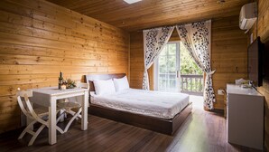 Une chambre dans une cabane en bois, avec un lit, une petite table sur laquelle se trouve une bouteille, et une chaise blanche.