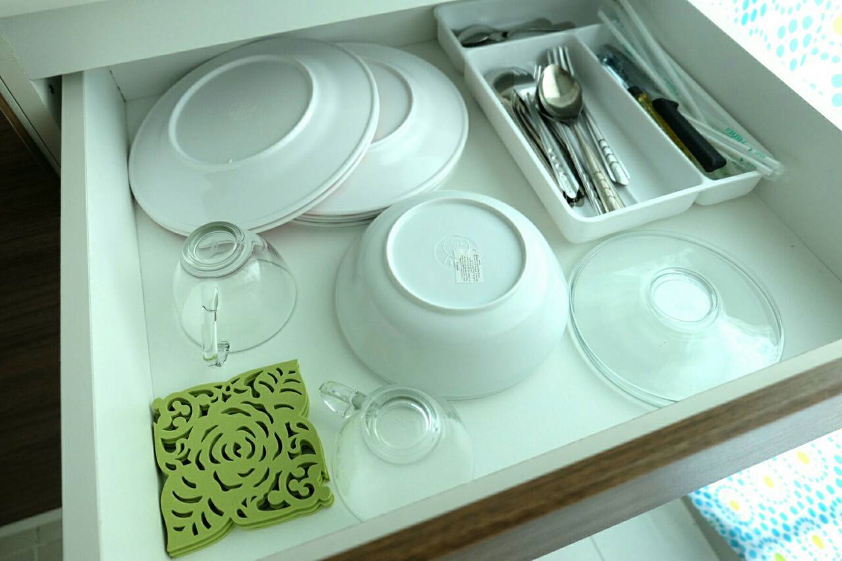 A drawer containing white plates, bowls, a glass pitcher, a spoon set, and a decorative item.