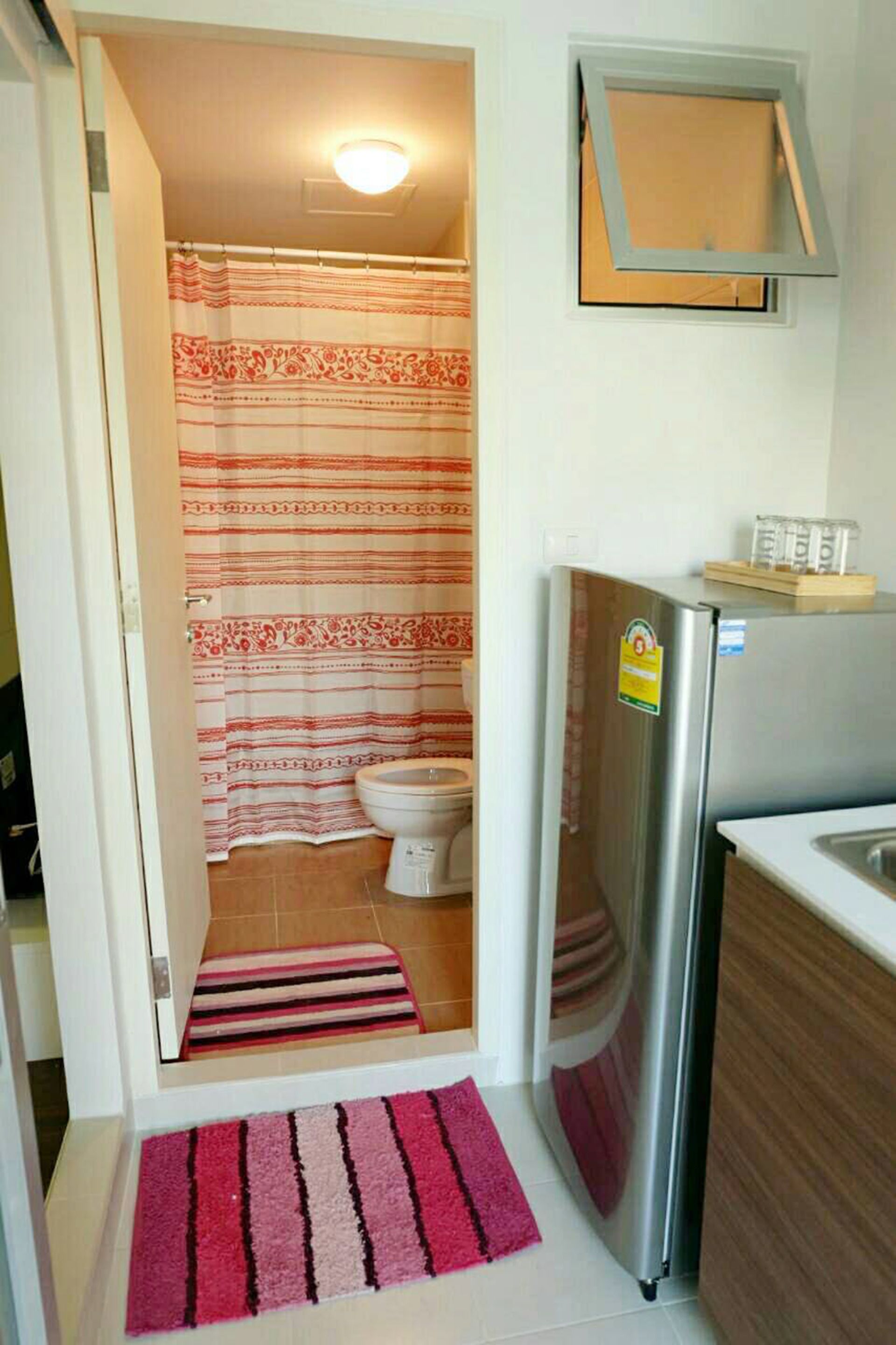 A compact bathroom with a shower curtain, toilet, and a refrigerator.