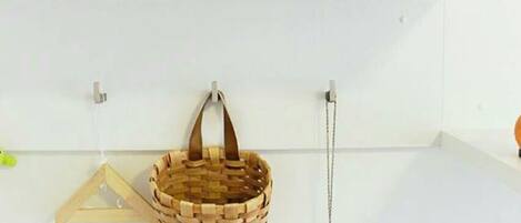 A white shelf with a painting, a blue flower in a white vase, a woven basket, and a hanging toy.