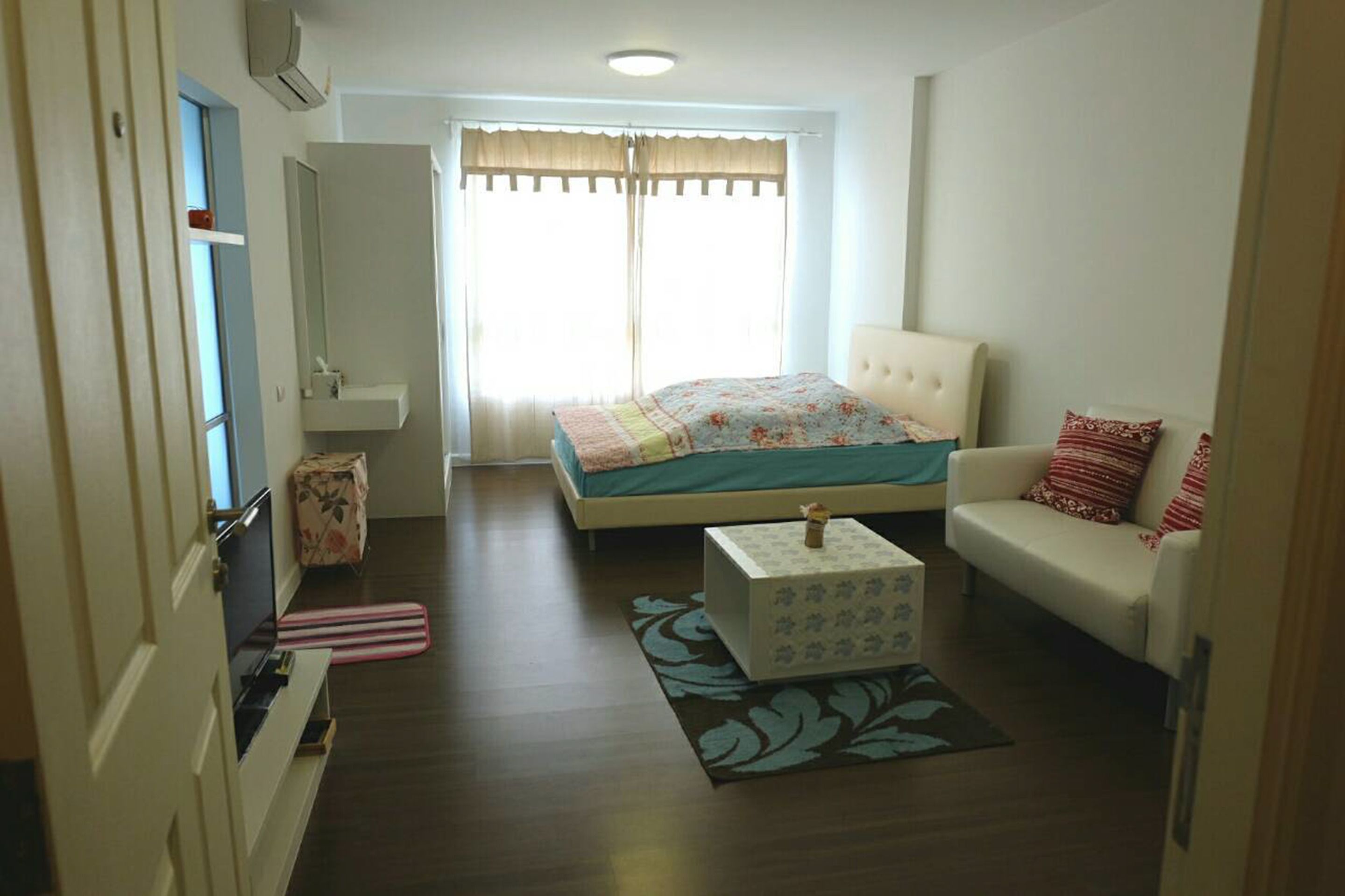 Ein Schlafzimmer mit Bett, einer Couch, einem kleinen Tisch, einem Koffer und einem Fenster mit Vorhängen.