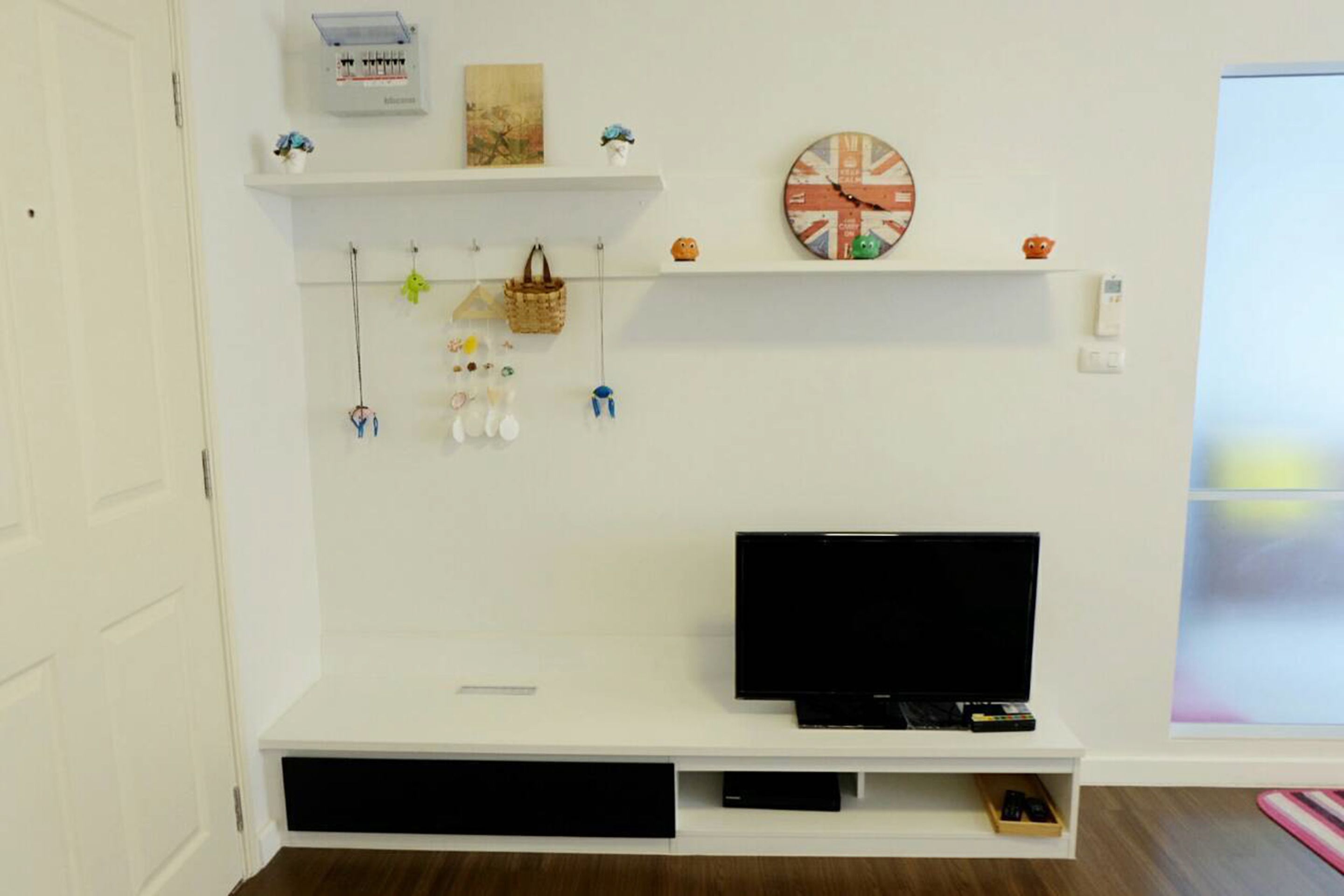 Een kamer met een witte entertainmentkast, een flatscreen-tv, planken met decoratieve items, en een raam met uitzicht.