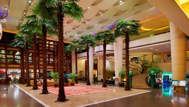 A spacious lobby with palm trees, a red carpet, and a staircase leading to upper floors. - Dongguan Huihua International Hotel (Dongguan)