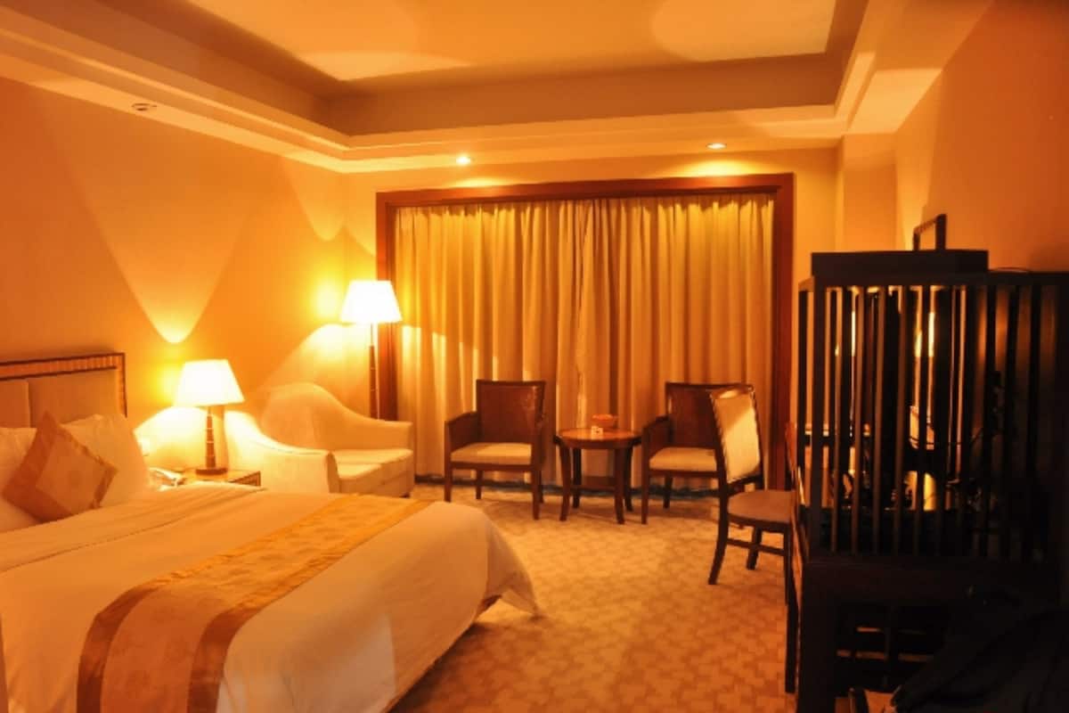 A hotel room with a large bed, two chairs, a small table, and a desk with a chair.