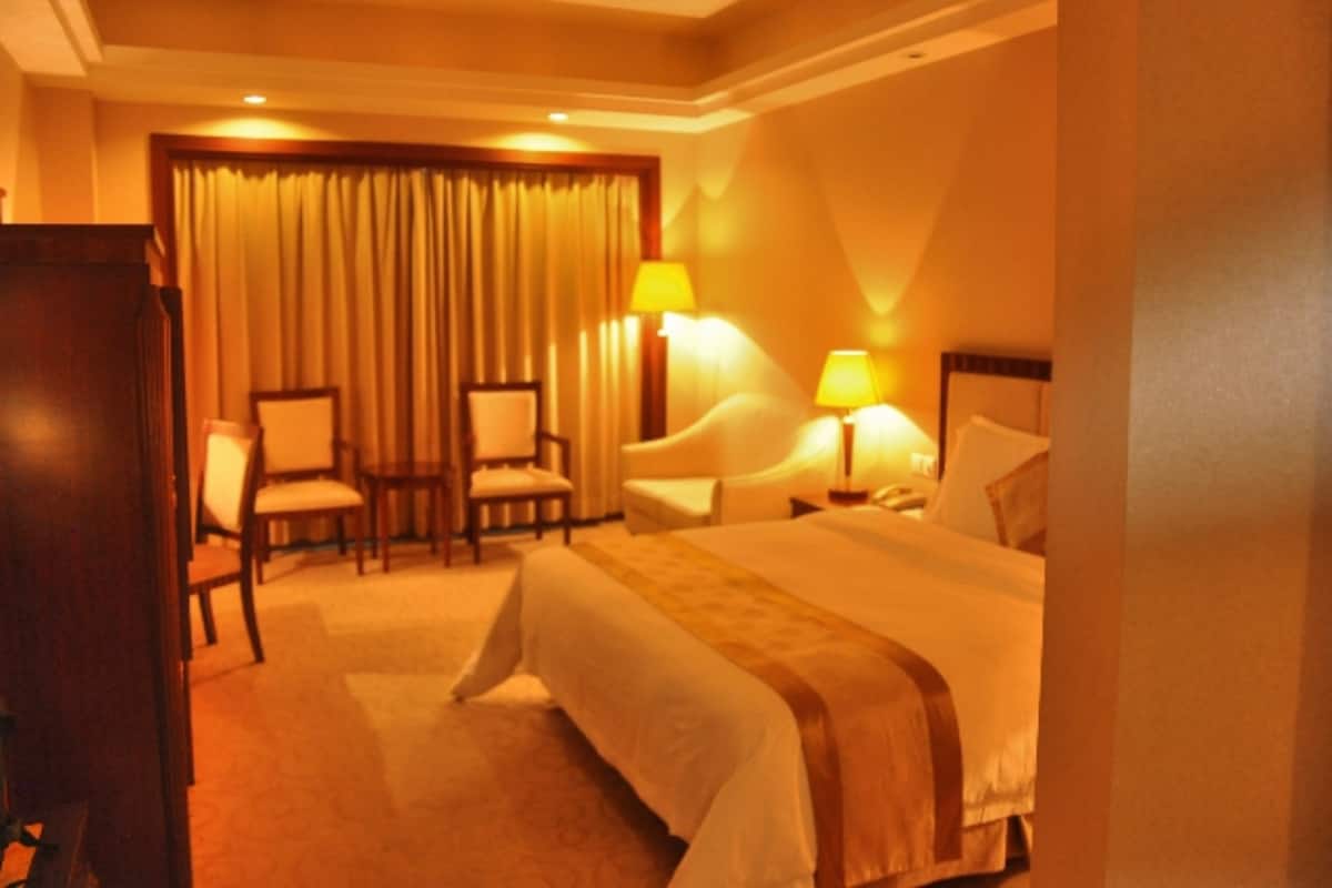 A hotel room with a bed, two chairs, a desk, and two lamps.