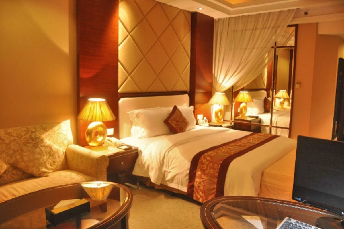 A hotel room with a large bed, a desk with a computer, a sofa, and two bedside lamps.