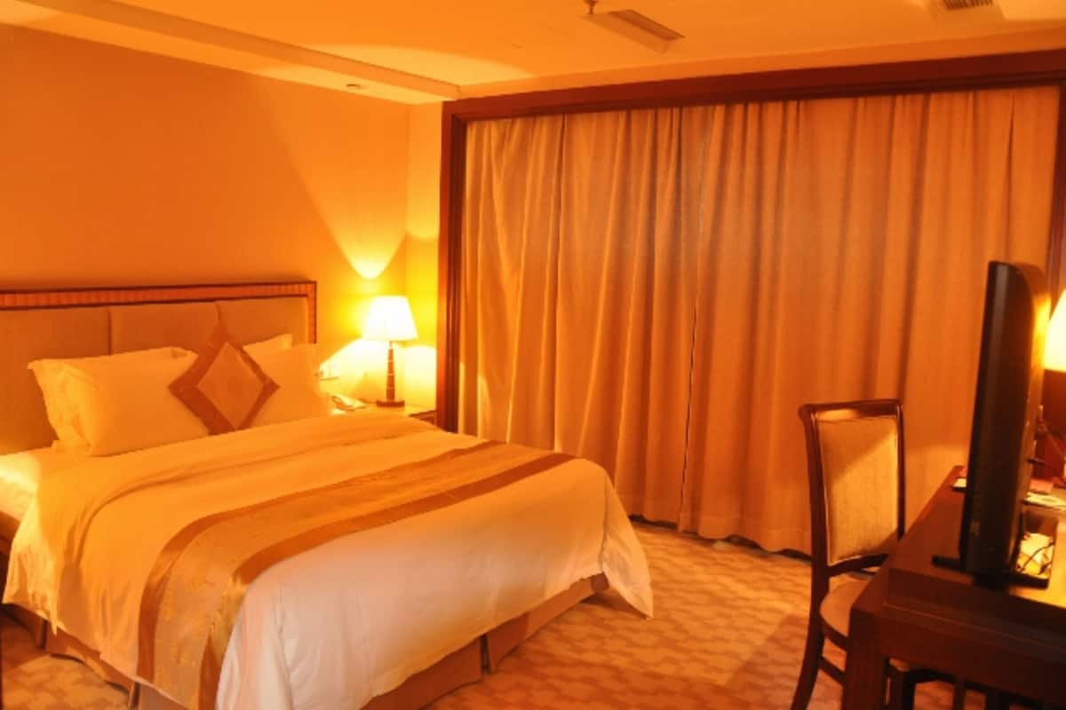A hotel room with a bed, a desk, a chair, a lamp, and a large window with curtains.