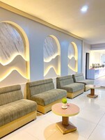 Uma área de estar moderna com sofás e uma mesa redonda, com design de parede em mármore e iluminação ambiente.