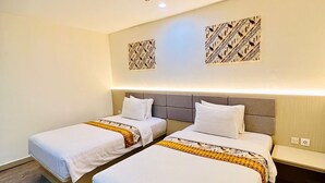 A hotel room with two beds, a grey headboard, and a wooden floor. - Belagri Hotel & Resto (Sorong)