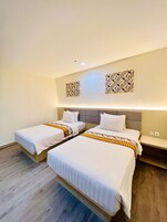 Quarto de hotel com duas camas, cabeceira cinza e piso de madeira.