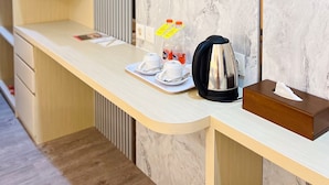 A modern hotel room with a marble wall, a flat-screen TV mounted above a wooden desk, a kettle, and a tissue box. - Belagri Hotel & Resto (Sorong)