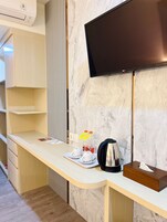 Quarto de hotel moderno com parede de mármore, TV de tela plana montada acima de uma escrivaninha de madeira, chaleira e caixa de lenços.
