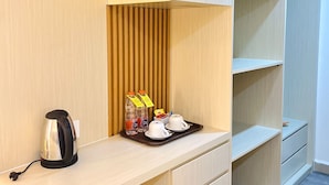 A hotel room with a wooden desk, a kettle, bottled water, and a tray with cups and a small box. - Belagri Hotel & Resto (Sorong)