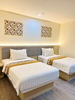 Quarto de hotel com duas camas, cabeceira cinza e painel de parede estampado.