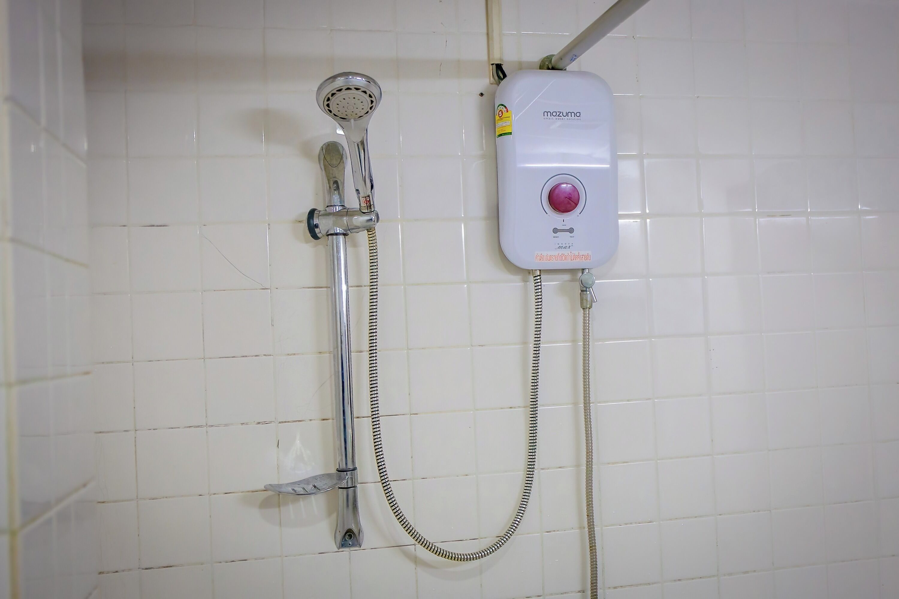 Un baño con paredes de azulejos blancos, una ducha con cabezal de ducha manual y un panel de control en la pared.