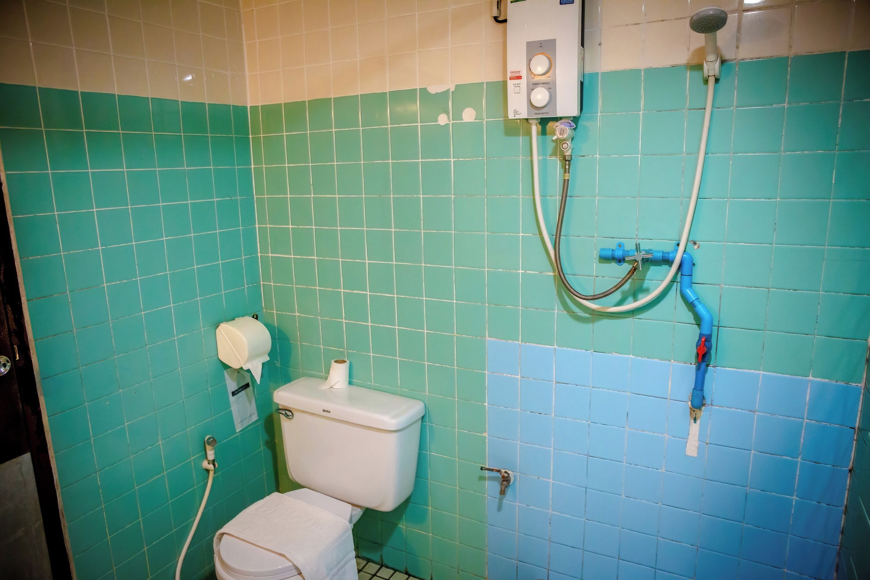 A bathroom with a toilet, a paper towel dispenser, and a shower with a control panel.