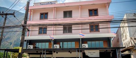 A pink building with multiple windows and flags, a sign for a coffee shop, and a visible entrance.