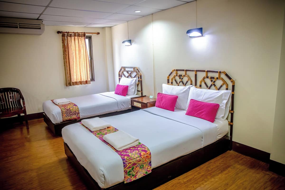 Habitación de hotel con dos camas, cada una con sábanas blancas y almohadas rosas, suelo de madera y una ventana con cortinas.