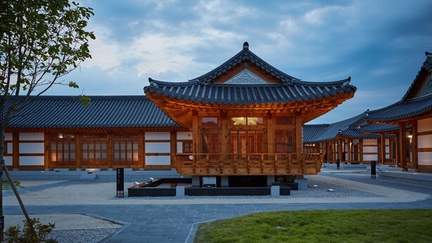 A traditional wooden building with a tiled roof, surrounded by a courtyard with stone pathways and a grassy area.