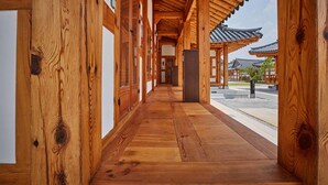 A wooden corridor with traditional architecture, leading to a courtyard with a tiled roof structure.