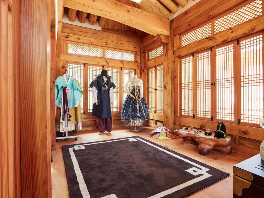 A traditional Japanese room with wooden walls and tatami flooring, featuring a tatami mat, a wooden table, and a display of traditional clothing.