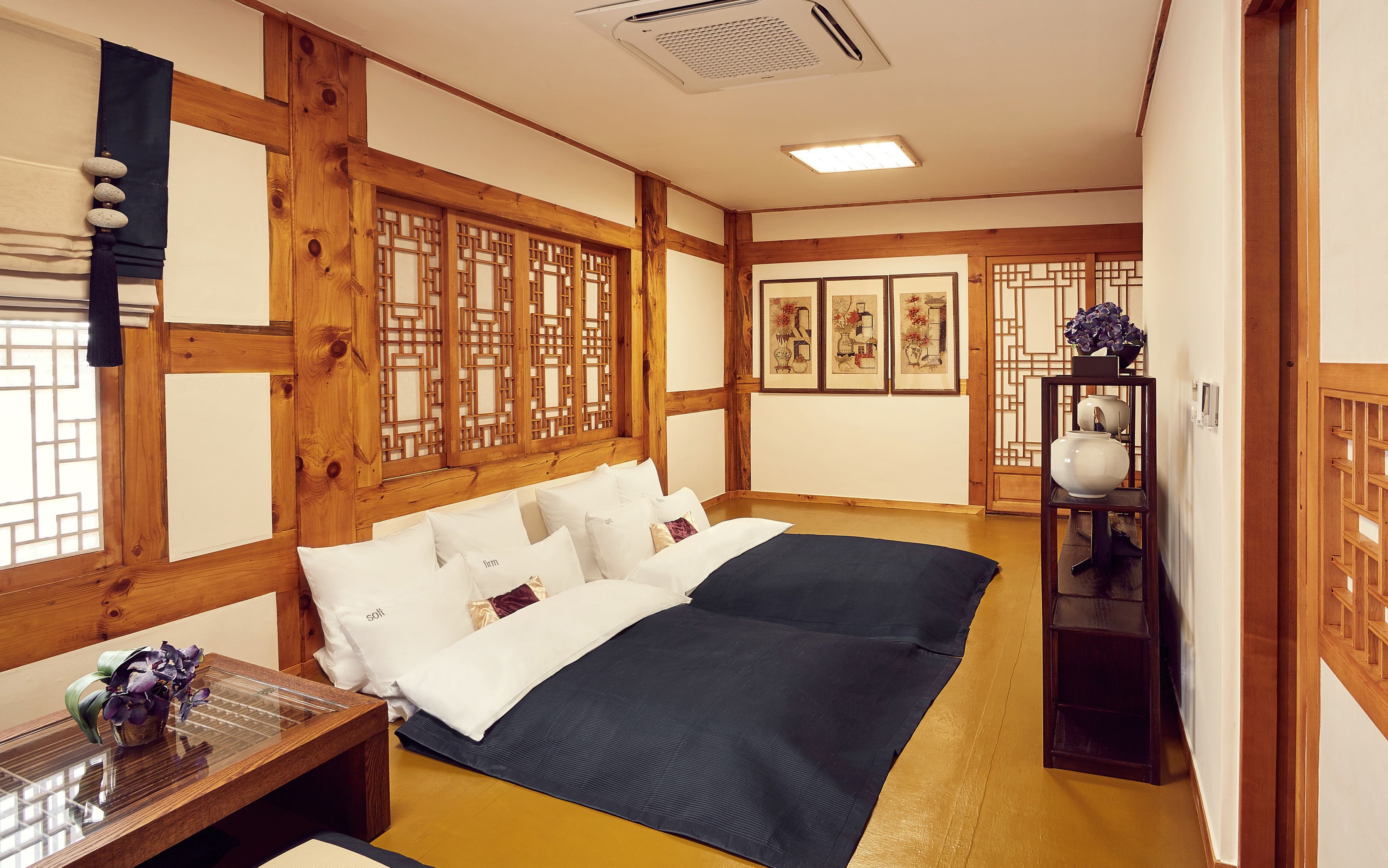 A traditional Japanese-style room with tatami flooring, a low wooden bed with white bedding, a shoji screen, and a small table with a vase of flowers.
