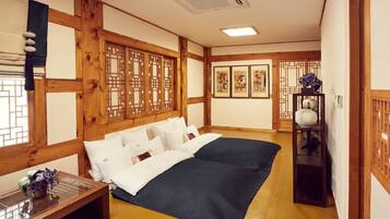 A traditional Japanese-style room with tatami flooring, a low wooden bed with white bedding, a shoji screen, and a small table with a vase of flowers.