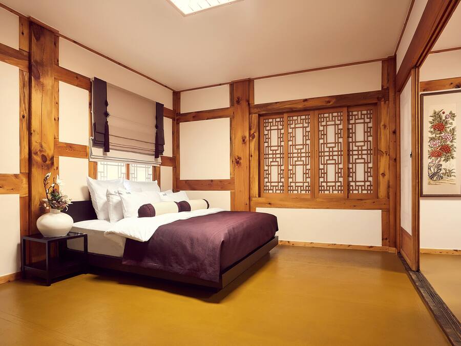 A traditional Japanese-style bedroom with tatami flooring, a low bed with a purple bedspread, wooden beams, and shoji screens.