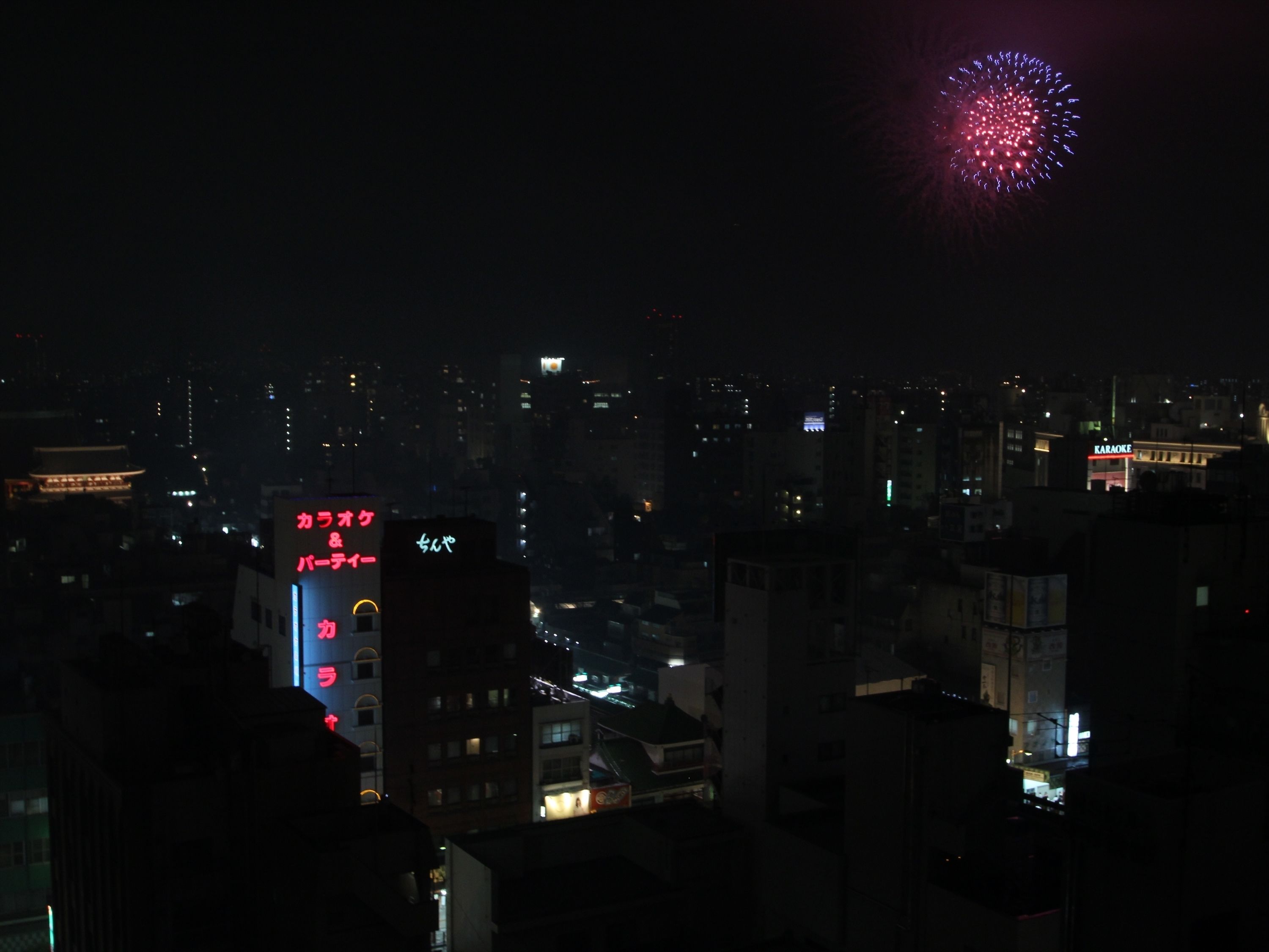 A nighttime cityscape with buildings and a visible sign for a karaoke bar.