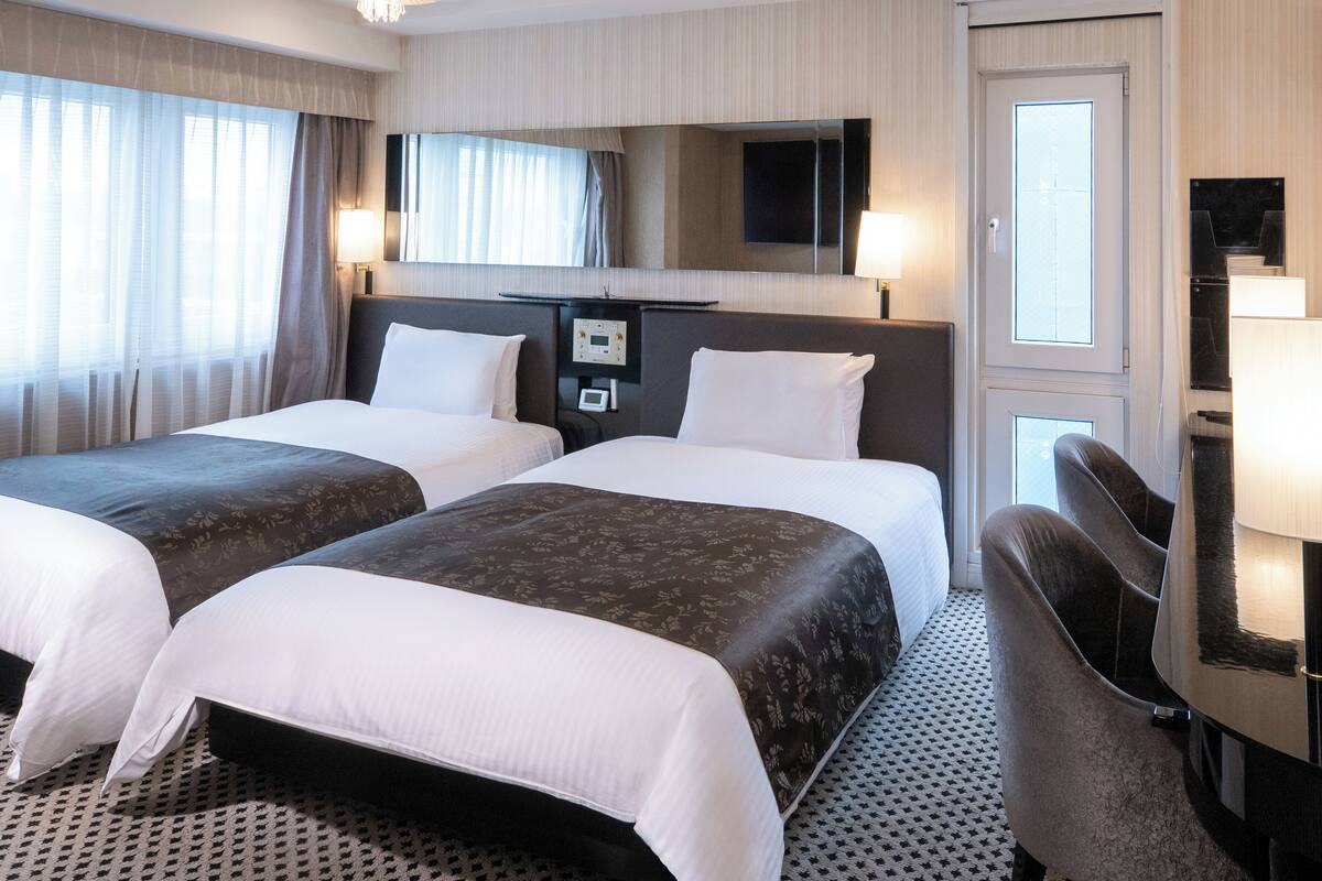 Une chambre d’hôtel avec deux lits, un bureau, une chaise, un miroir et un téléviseur.
