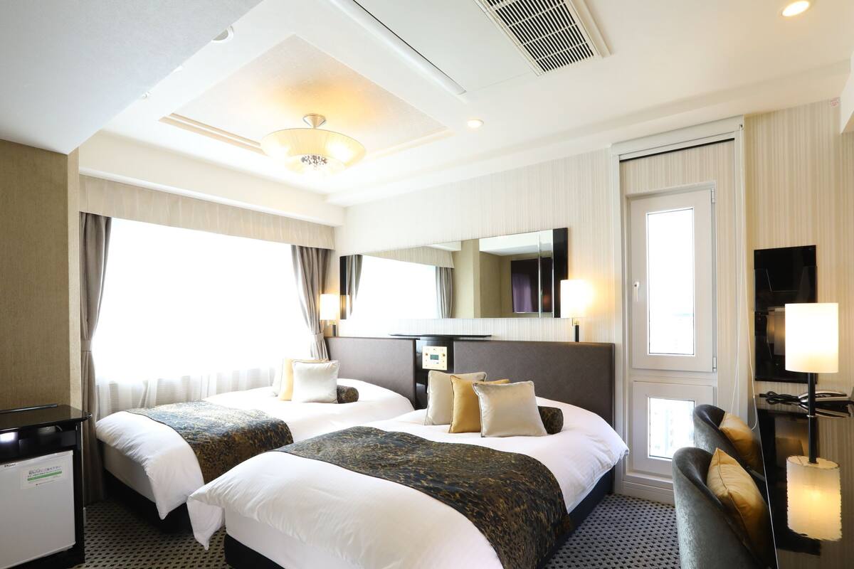 Une chambre d’hôtel avec deux lits, un bureau, une chaise, un miroir et une fenêtre.