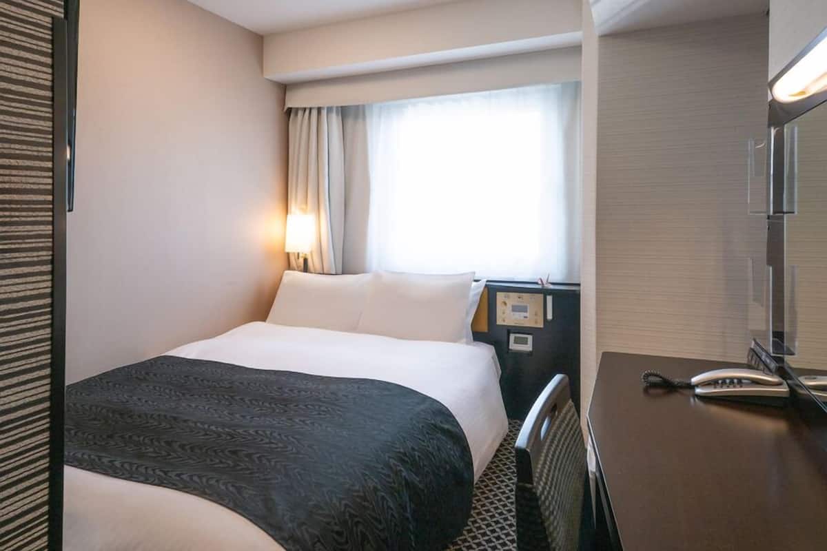 Ein Hotelzimmer mit Bett, Schreibtisch, Telefon und einem Fenster mit Vorhängen.